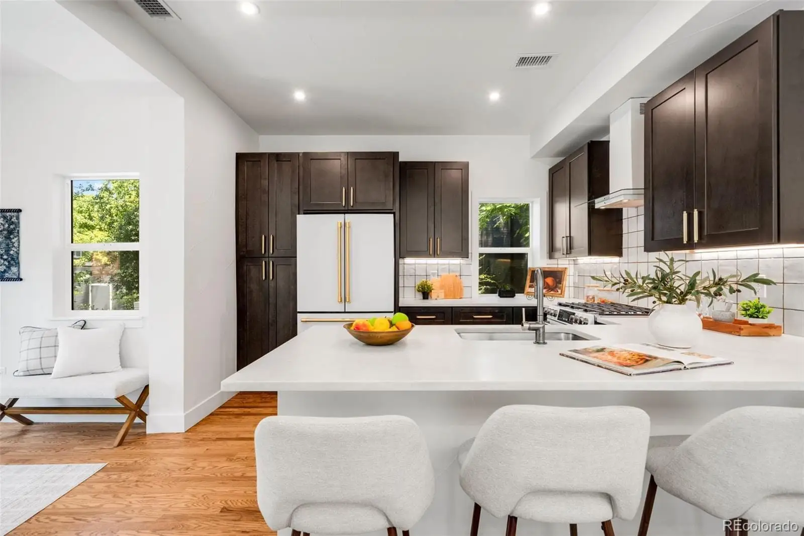 A kitchen with a sink dishwasher a stove and chairs with wooden floor at 2343 Dahlia Street